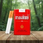 ซองบุหรี่กรองทิพย์ 90 แบบซองอ่อนสีแดงเอกลักษณ์ พร้อมมวนบุหรี่ก้นกรองสีส้ม วางบนโต๊ะไม้ในป่า