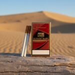 ซองบุหรี่ Gudang Baru International 20 สีแดงตัดทองหรูหรา วางบนขอนไม้ในทะเลทราย แสงแดดสีทอง