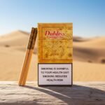 ซองบุหรี่ Dubliss Caribbean ลายแผนที่โบราณสีทอง วางบนขอนไม้กลางทะเลทราย แสงแดดอุ่น