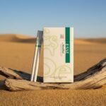 ซองบุหรี่ ESSE Menthol สีขาวแถบเขียว วางบนขอนไม้กลางทะเลทราย แสงแดดอุ่น