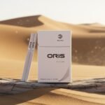 ซองบุหรี่ Oris Nano Silver และมวนนาโนสลิม วางบนขอนไม้กลางทะเลทราย แสงแดดสีทอง