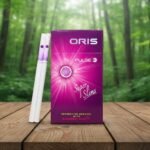ซองบุหรี่ Oris Pulse Menthol with Blueberry สีม่วงชมพูและมวนซุปเปอร์สลิม วางบนโต๊ะไม้ฉากหลังป่า