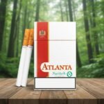 ซองบุหรี่ Atlanta Switch Menthol สีขาวแถบแดง พร้อมมวนบุหรี่วางบนโต๊ะไม้ ท่ามกลางบรรยากาศป่าเขียวขจี