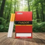 ซองบุหรี่ Napoli Red Limited Edition สีแดงดีไซน์หรูวางคู่กับมวนบุหรี่บนโต๊ะไม้ ฉากหลังป่าสีเขียว