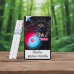 ซองบุหรี่ D&J Double Switch วางบนโต๊ะไม้ในบรรยากาศป่าเขียวขจี แสดงดีไซน์ซองสีดำและมวนบุหรี่ 2 เม็ดบีบ