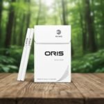 ซองบุหรี่ Oris Nano Silver สีขาวดีไซน์มินิมอล วางบนโต๊ะไม้พร้อมมวนบุหรี่นาโนสลิม ฉากหลังเป็นป่าธรรมชาติ