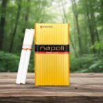 บุหรี่ Napoli Gold ซองสีทองหรูหรา วางคู่กับมวนบุหรี่บนโต๊ะไม้ ท่ามกลางบรรยากาศป่าเขียวขจี