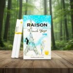 บุหรี่ Raison French Yogo ซองสีขาวลายหอไอเฟลและแมวดำ วางคู่กับมวนบุหรี่บนโต๊ะไม้ ฉากหลังเป็นป่า